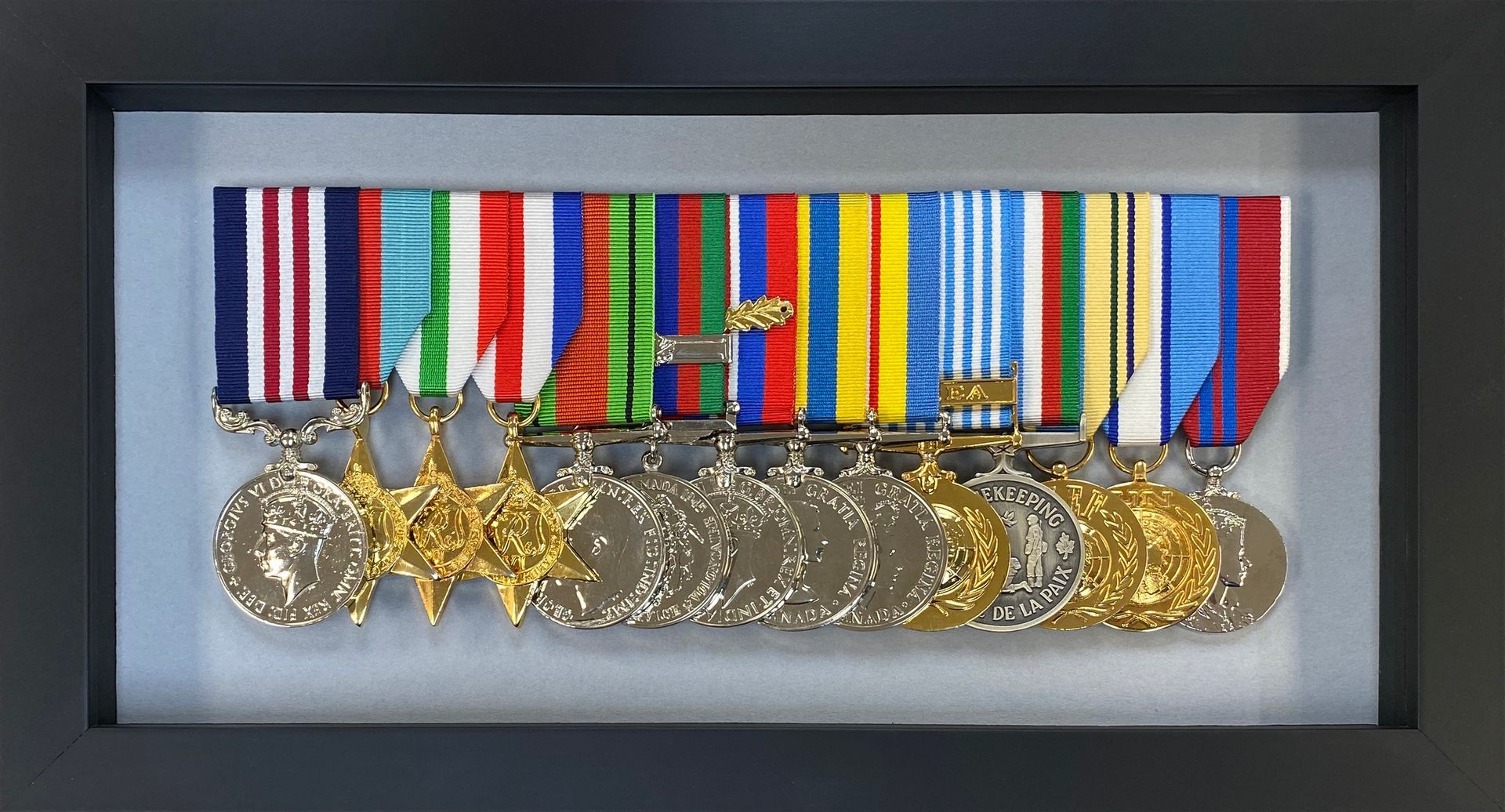 Military medals with colourful ribbons arranged in a black shadow box with a light grey backing