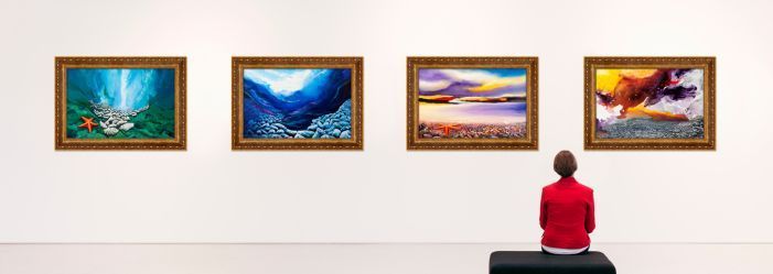 A woman is sitting on a bench in front of a wall of paintings.