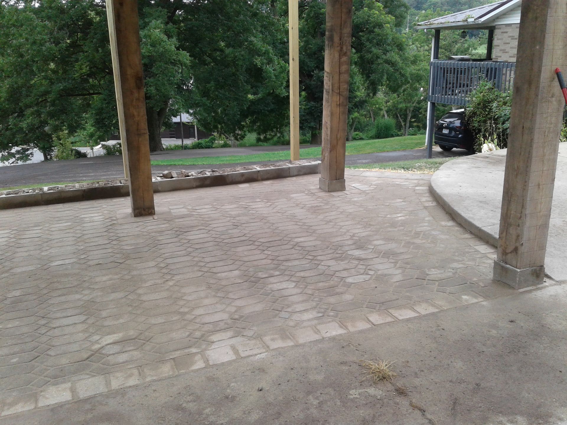 Concrete patio area with pillars, bordering a curved edge, with trees in the background.