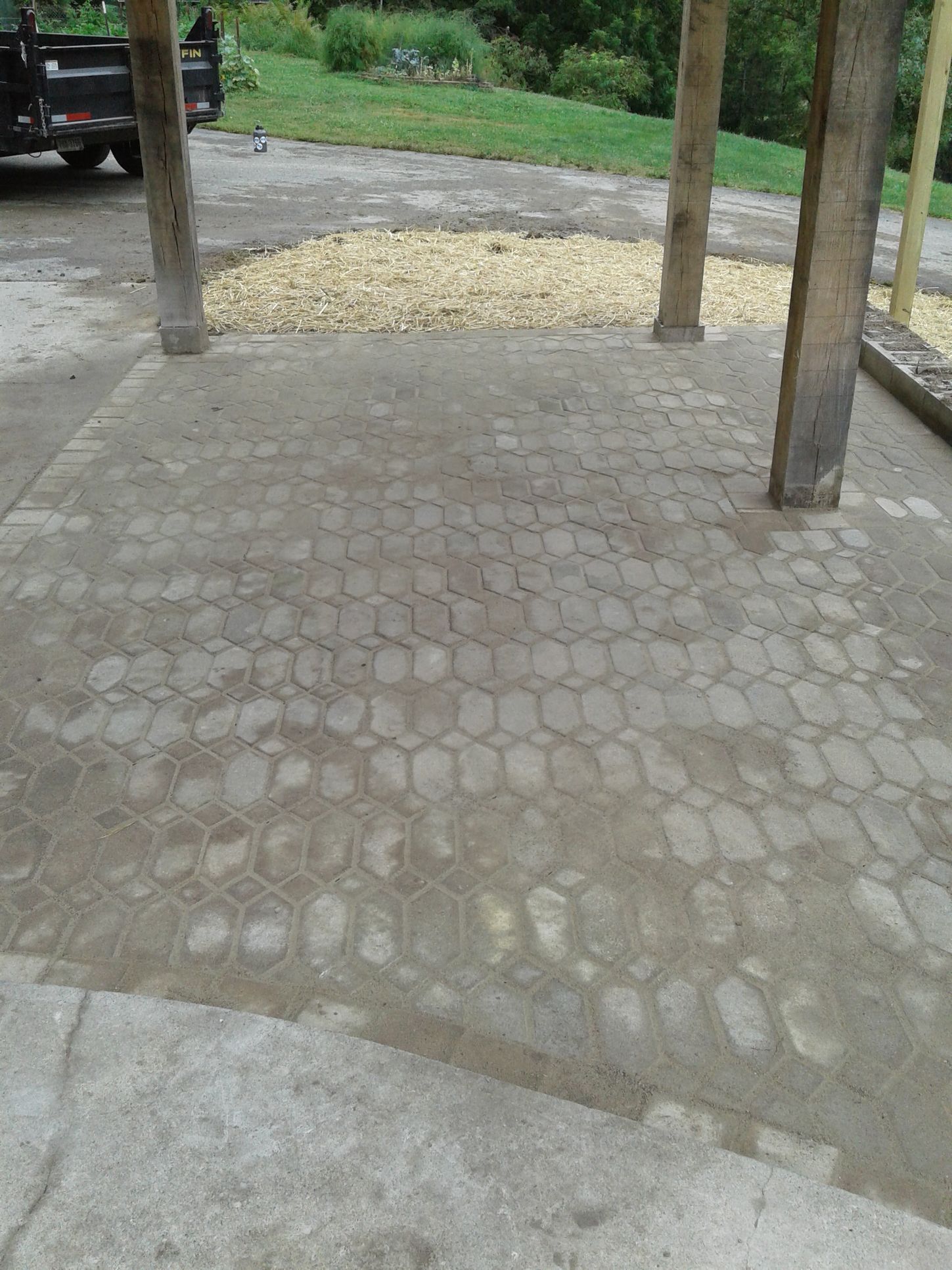 Paved area with hexagonal pattern under wooden supports. A truck is partially visible.