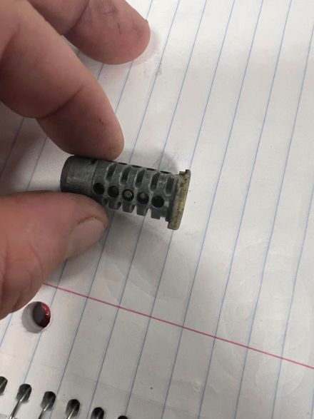 Hand holding a small gray plastic part on lined notebook paper