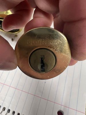 Close-up of a brass deadbolt lock held in a hand over lined notebook paper.