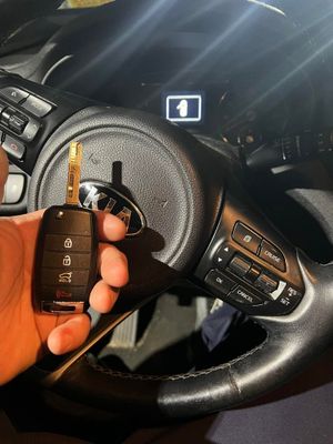 Hand holding a black car key fob near a steering wheel inside a vehicle