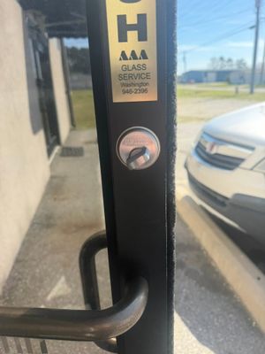 Close-up of a black door handle and lock with an AAA Garage sticker on a glass door, car visible outside.