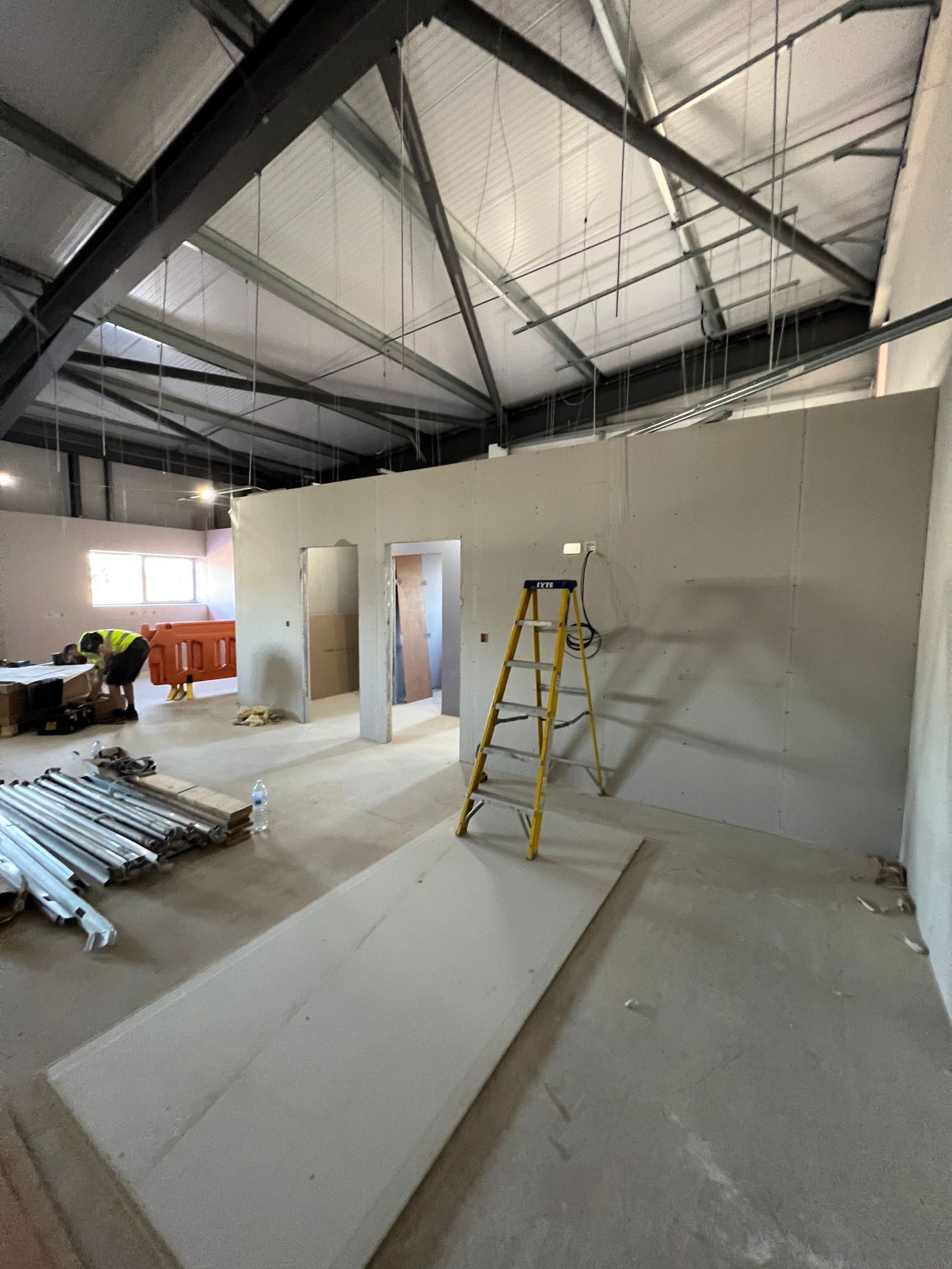 Interior of unfinished warehouse with exposed beams, drywall, ladder, and stacked materials on the floor