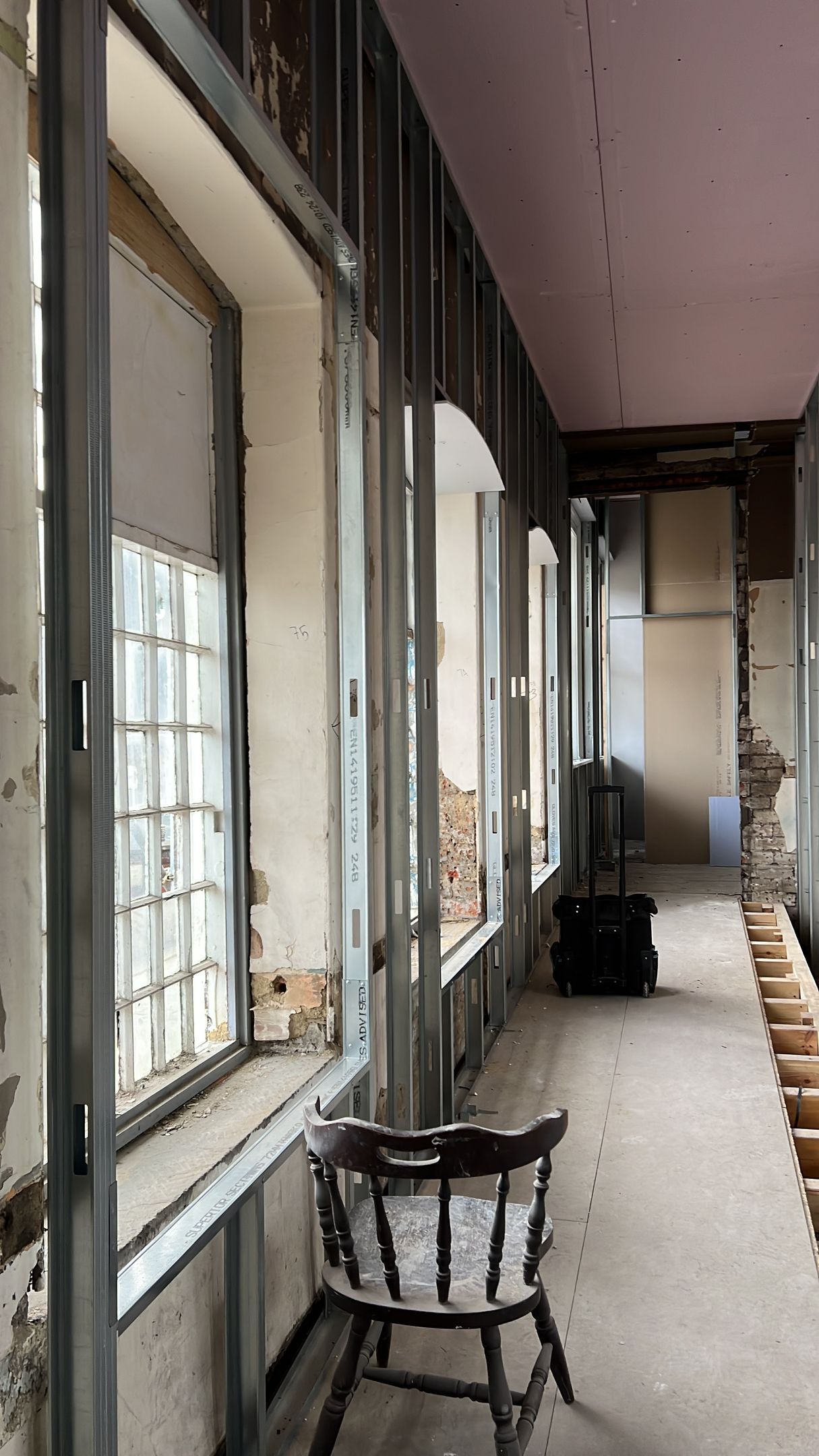 Narrow unfinished hallway with exposed walls, large windows, and a chair near the foreground.