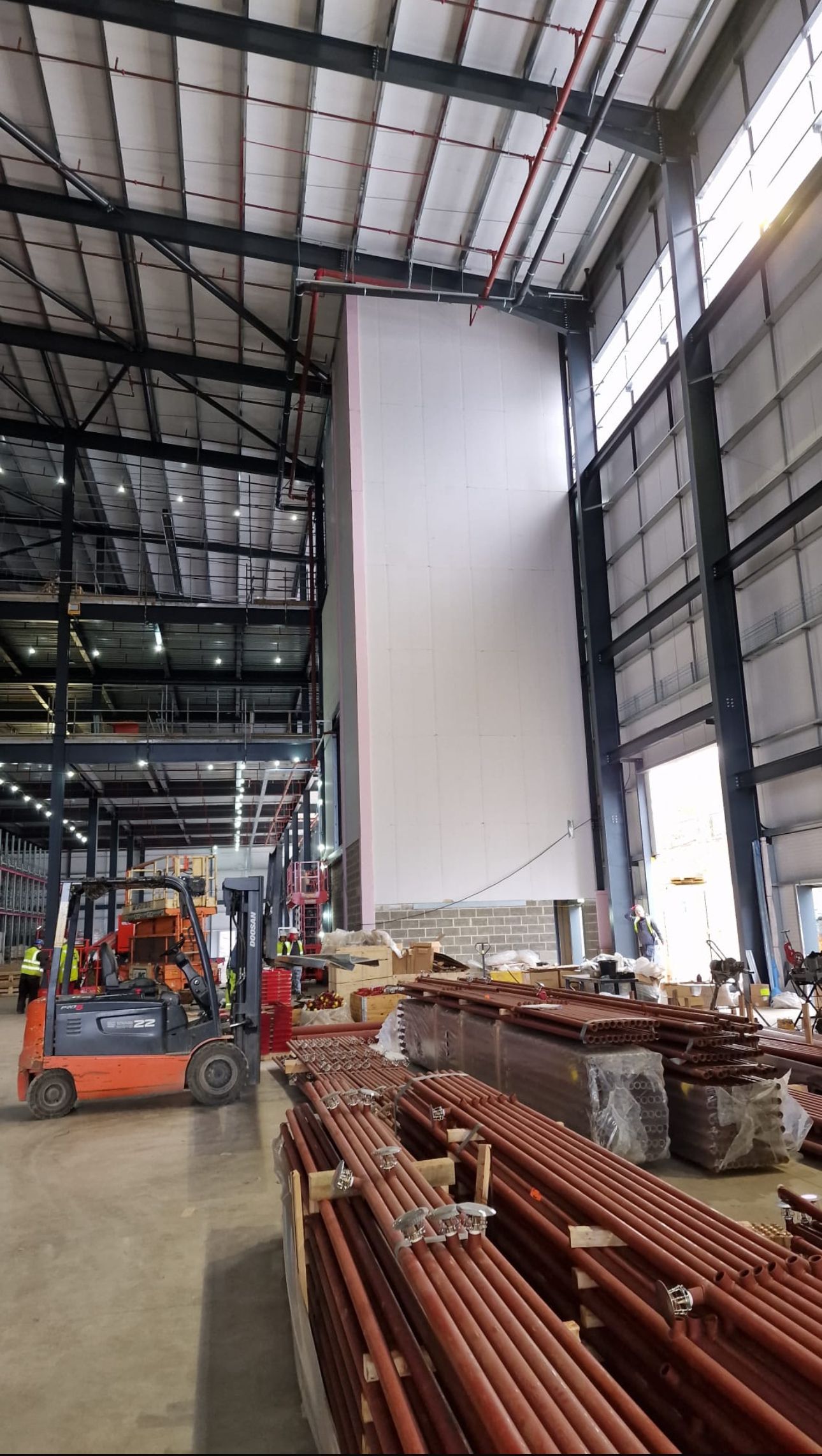 Large industrial warehouse with stacked metal beams, construction materials, and a forklift inside.