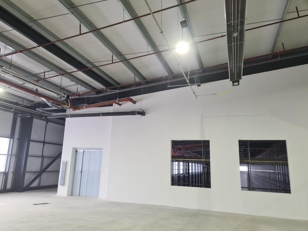 Empty warehouse interior with white walls, exposed ceiling beams, and two windows.