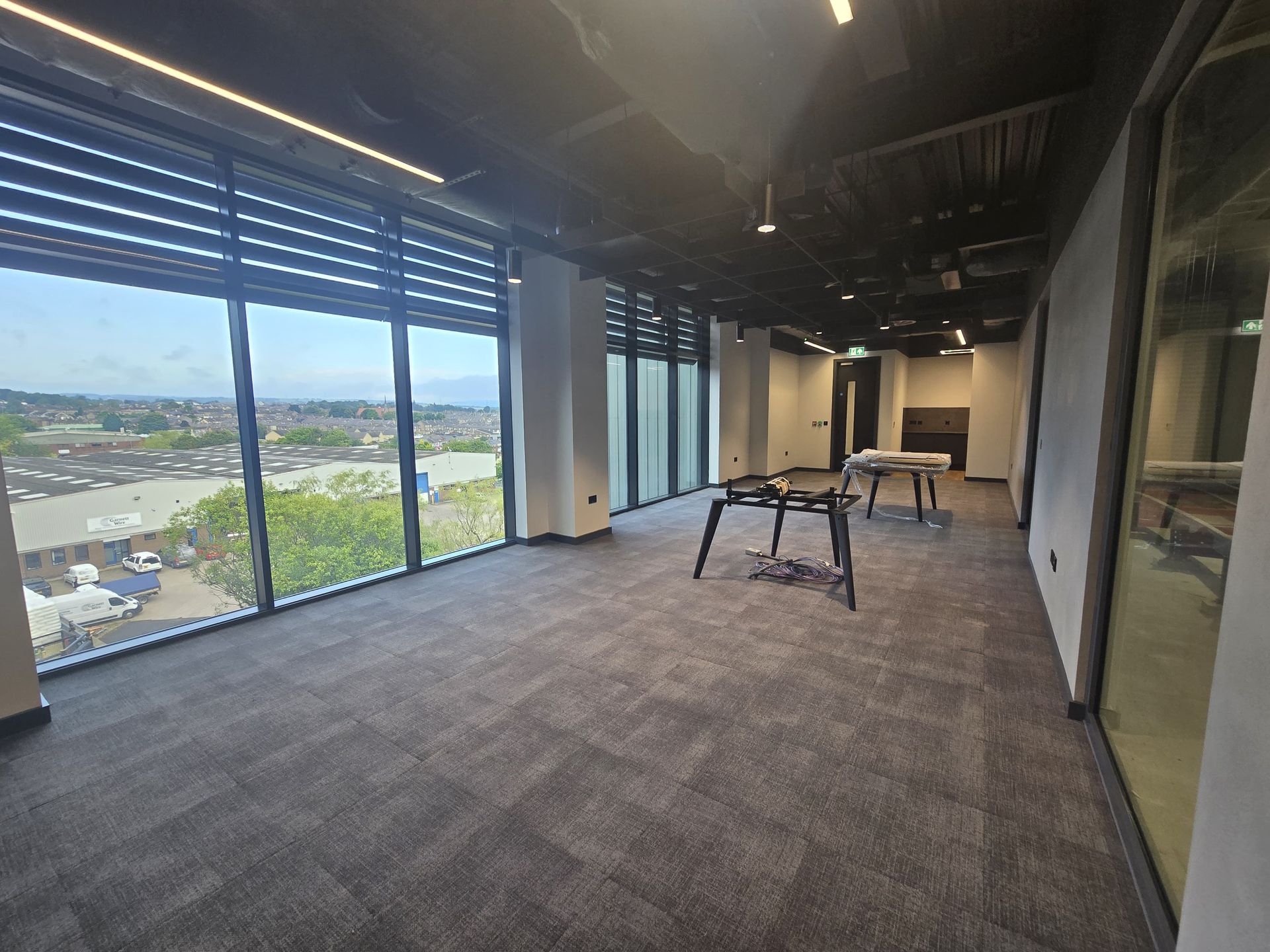 Empty modern office space with carpeted floor, large windows, and a city view.
