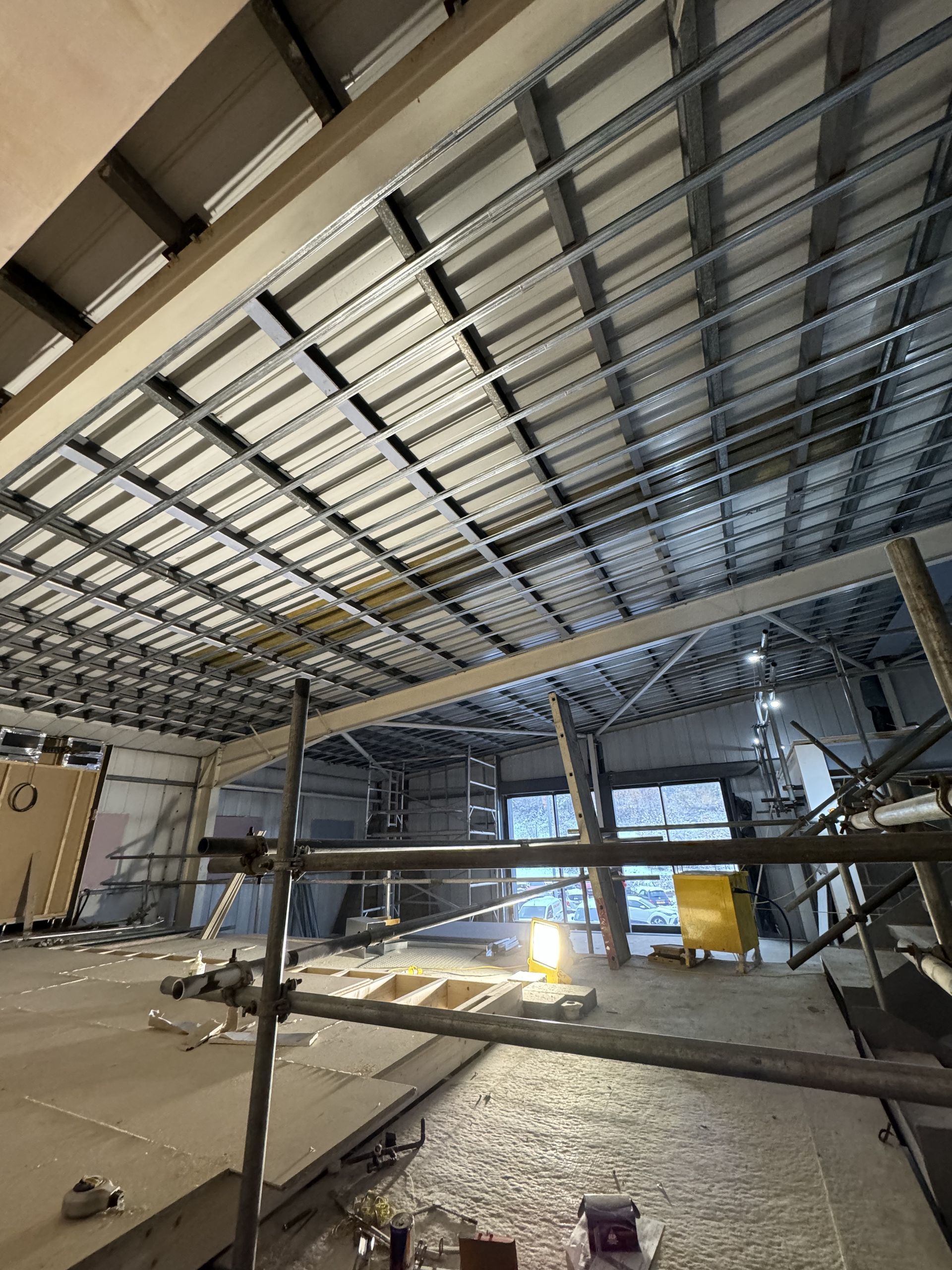 Indoor construction site with steel framing, scaffolding, and bright work lights on a concrete floor