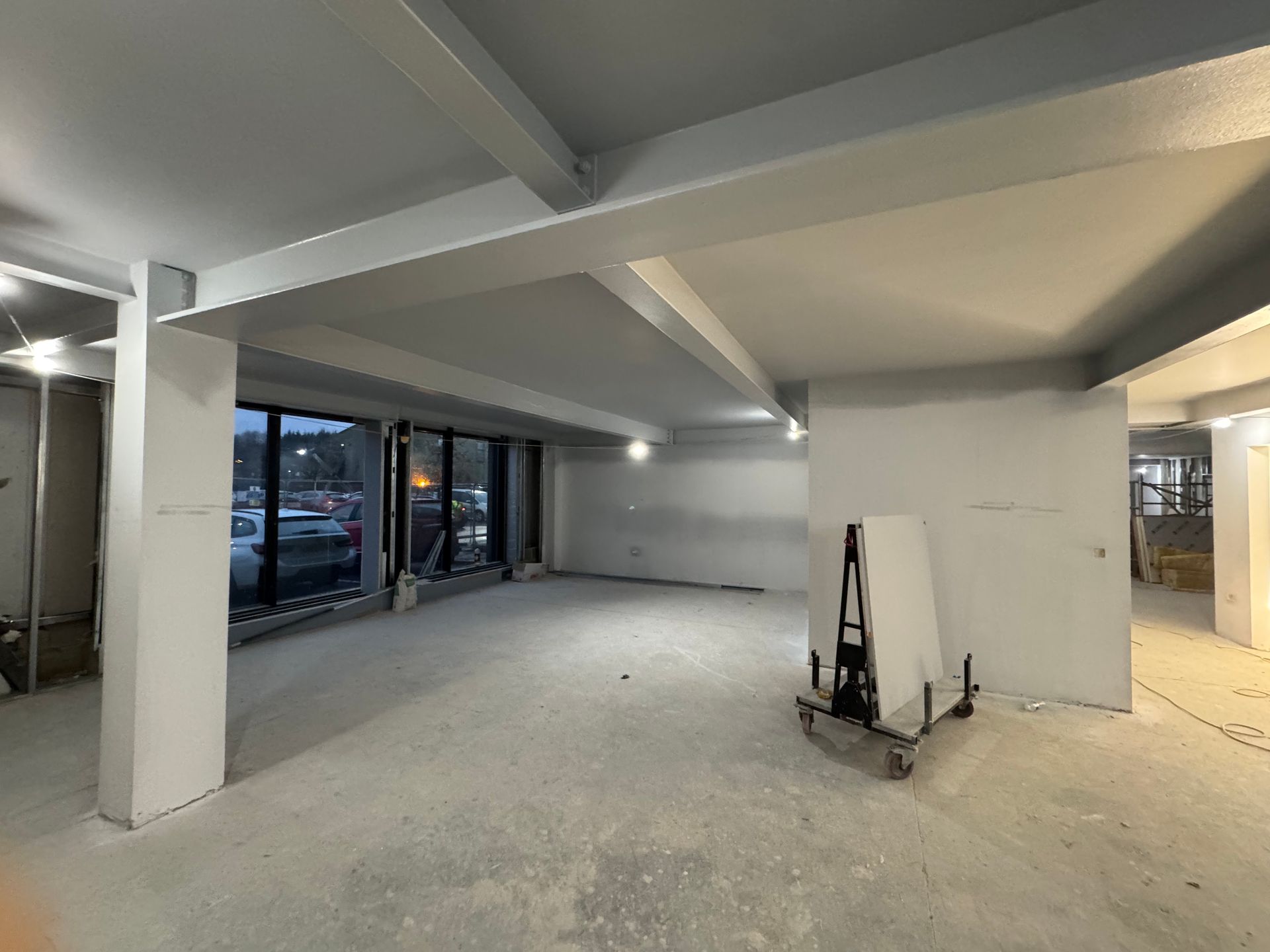 Empty unfinished retail space with white columns, exposed ceiling beams, and large front windows