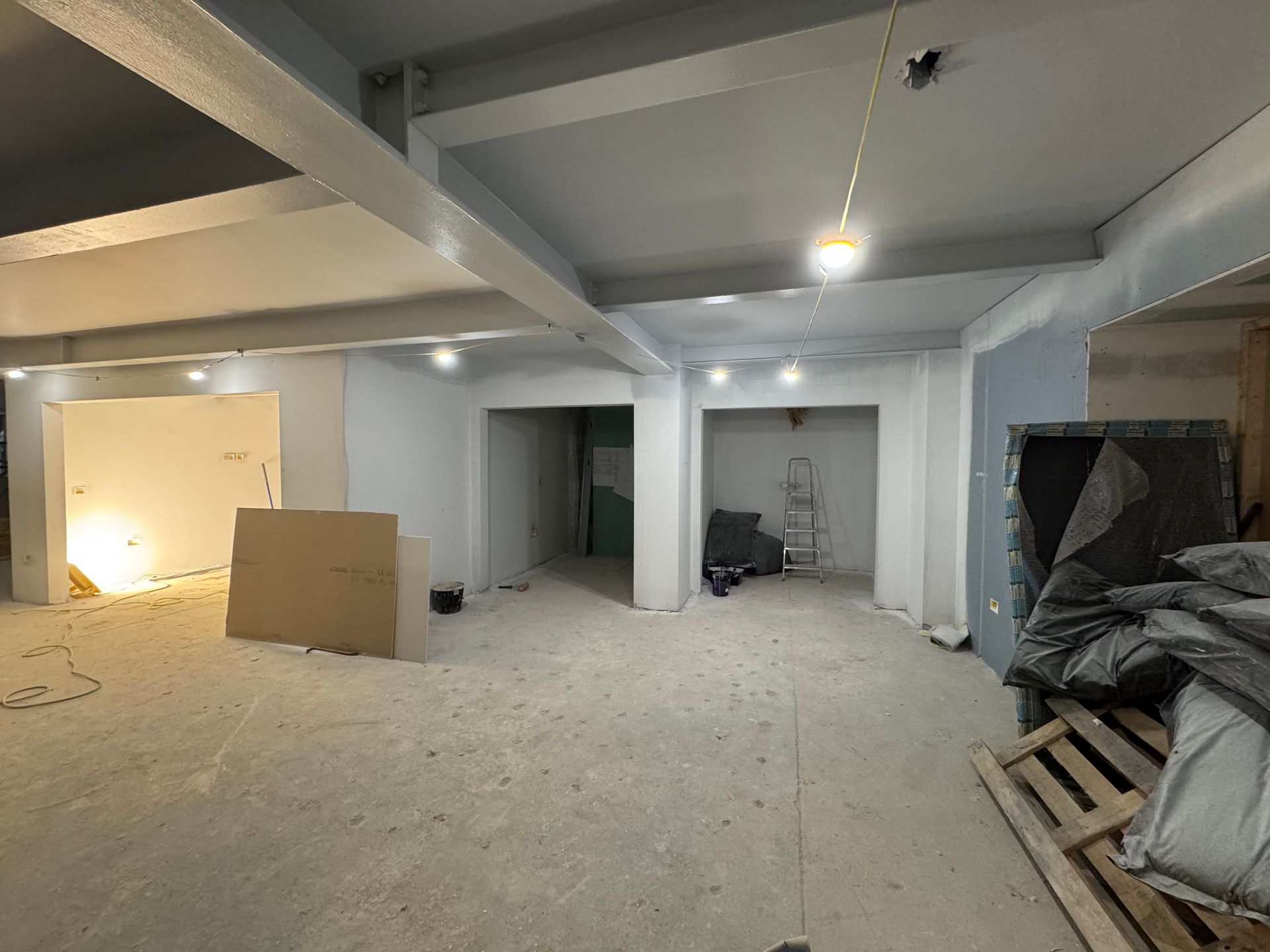 Renovation site with unfinished room, exposed ceiling lights, drywall, and construction materials scattered on the floor