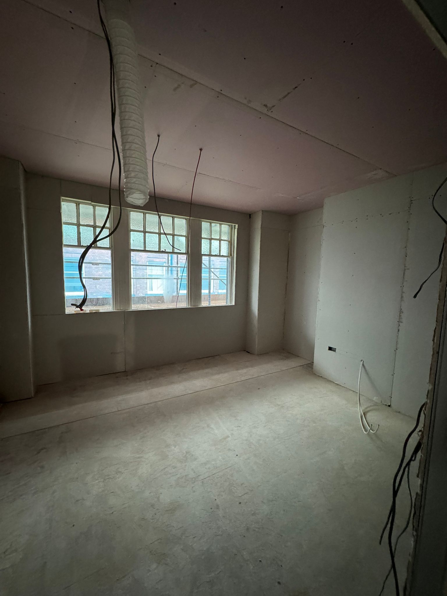 Bare unfinished room with white walls, ceiling seams, and a window letting in daylight.