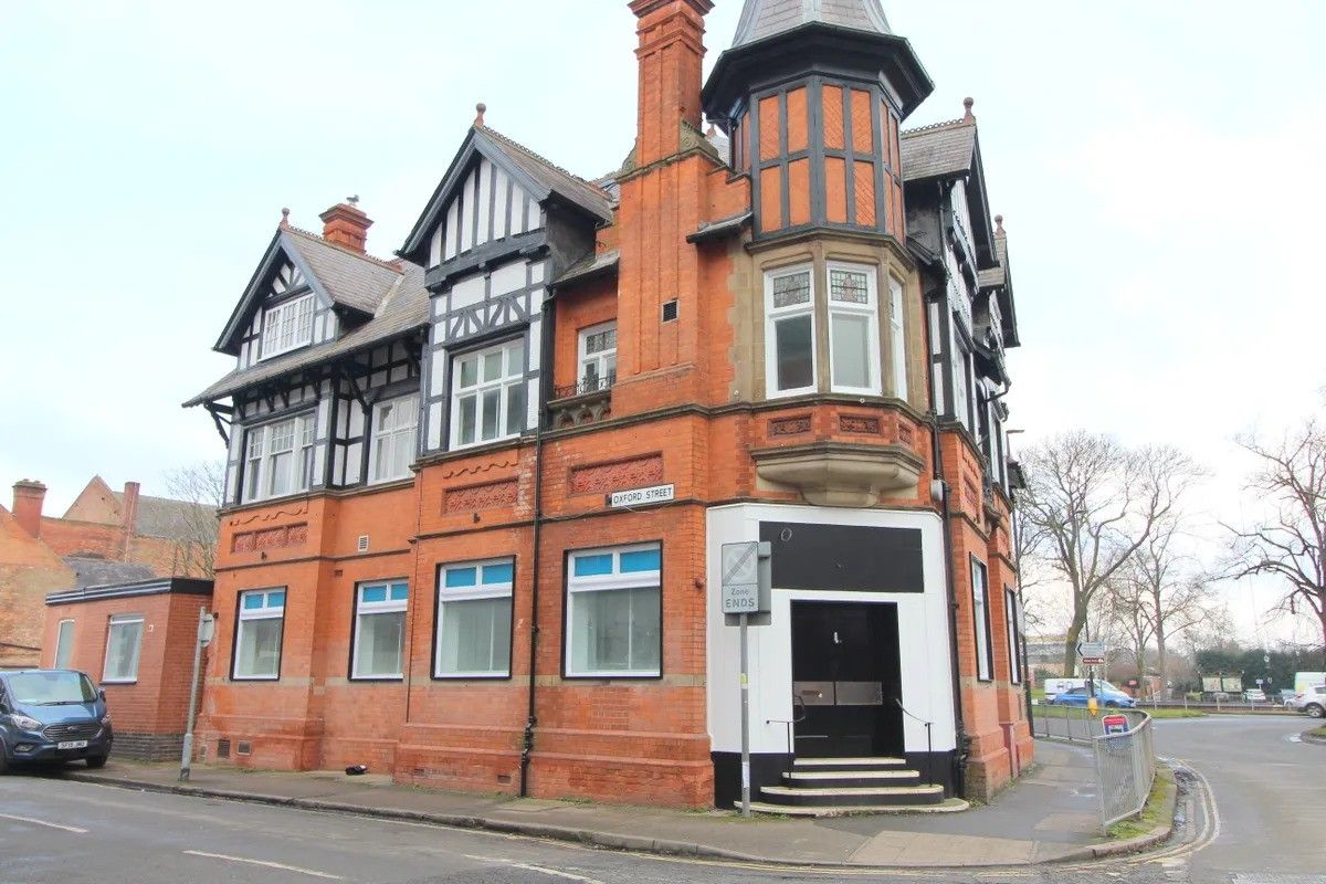 Red-brick corner building with white trim and black gables on a street under an overcast sky