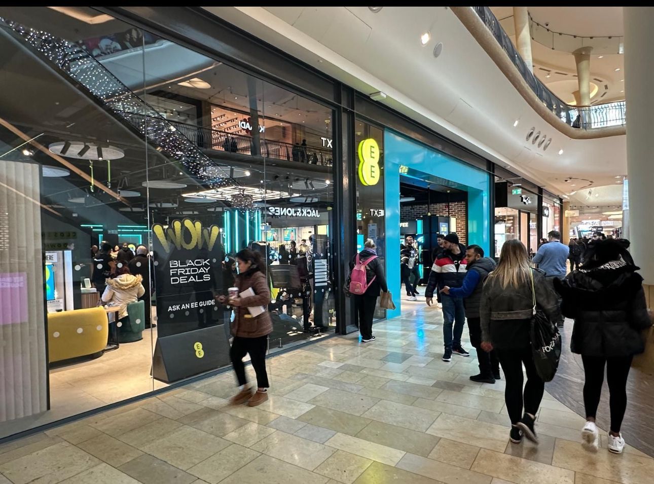 Shoppers walking through a modern mall corridor with illuminated storefronts and glass railings