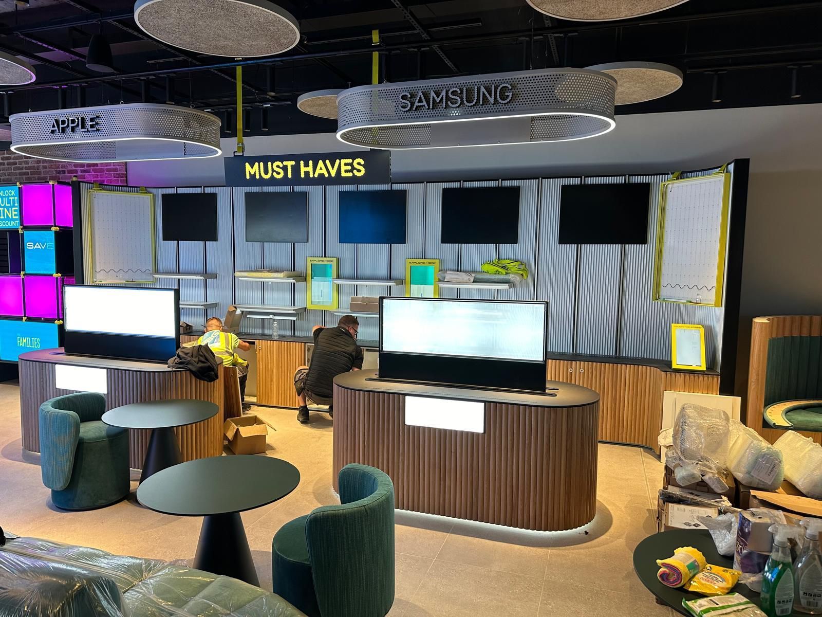 Retail display area with monitors, neon accents, and lounge seating under “MUST HAVES” signage