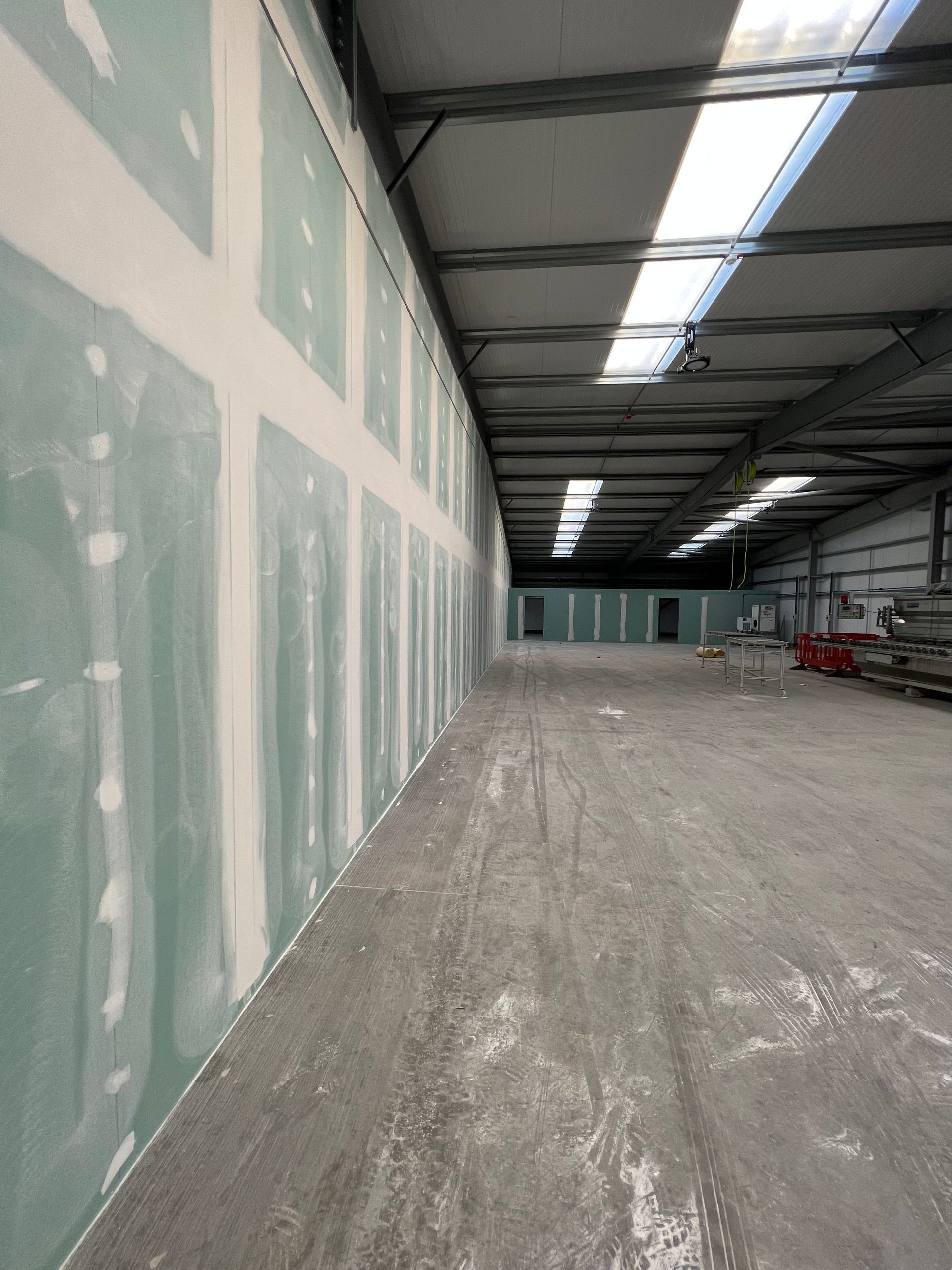 Large unfinished warehouse interior with drywall walls, concrete floor, and overhead lights
