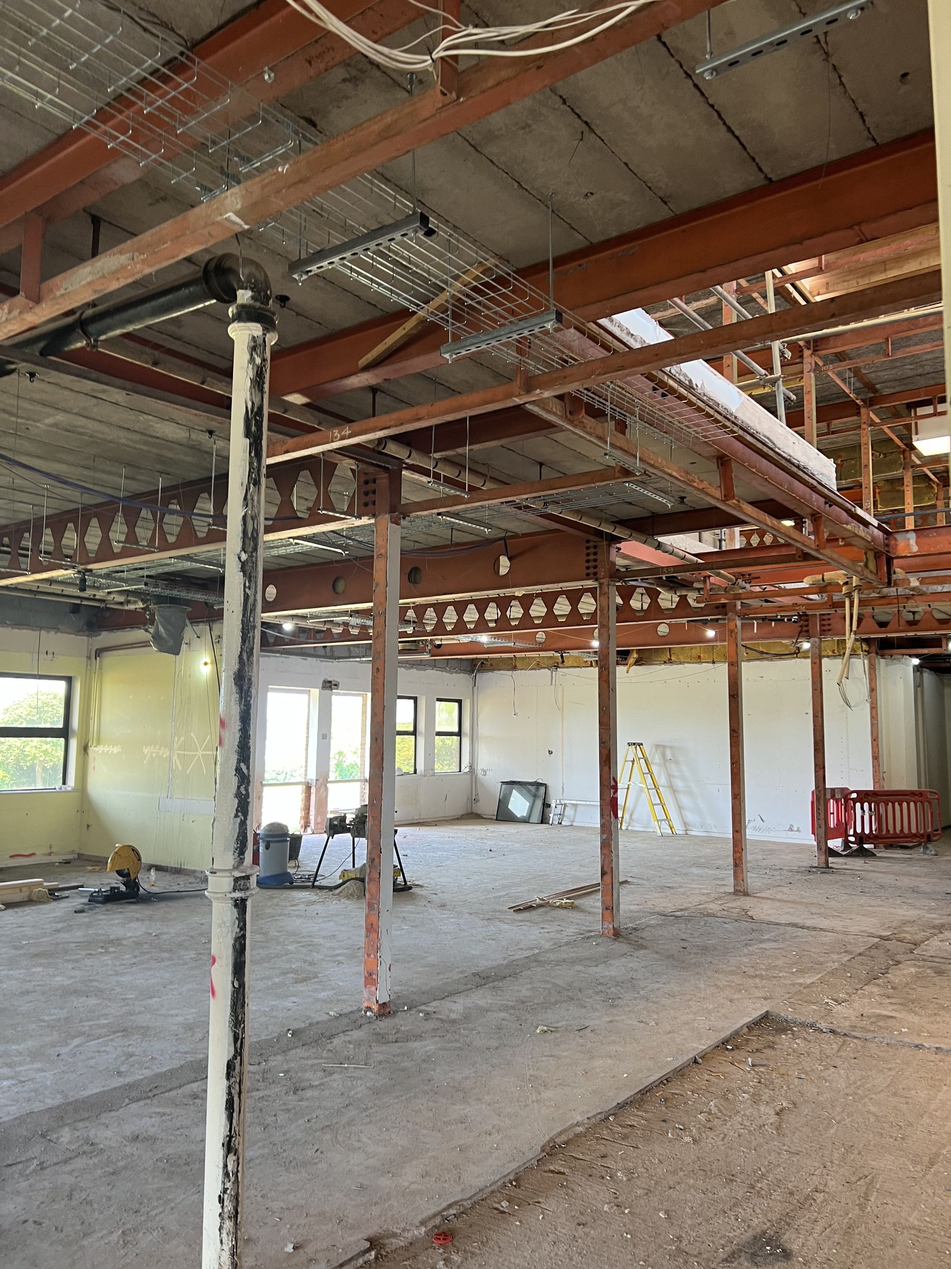 Empty industrial interior with exposed beams, pipes, and unfinished concrete floors under renovation