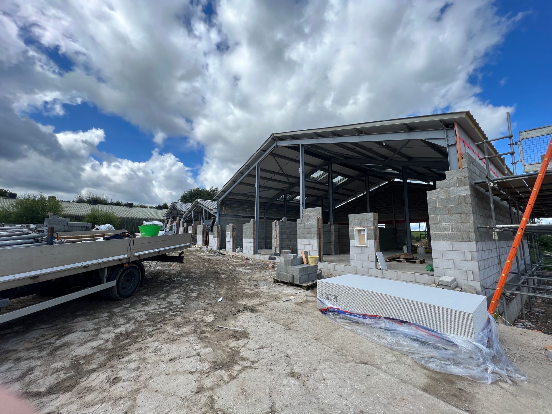 Partially built concrete structure with steel roof frame on a construction site under cloudy sky