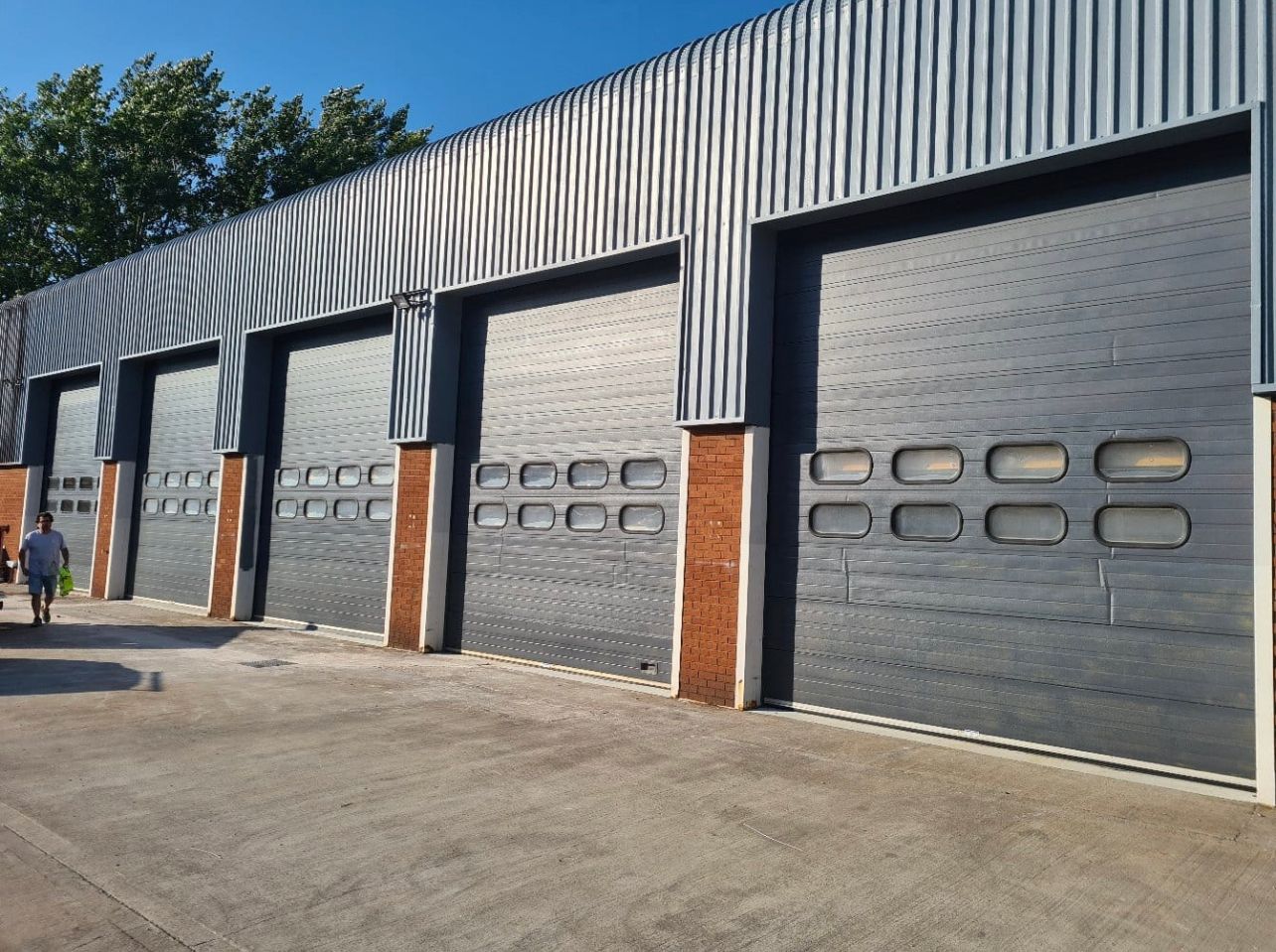 Row of gray industrial garage doors on a brick building under a blue sky