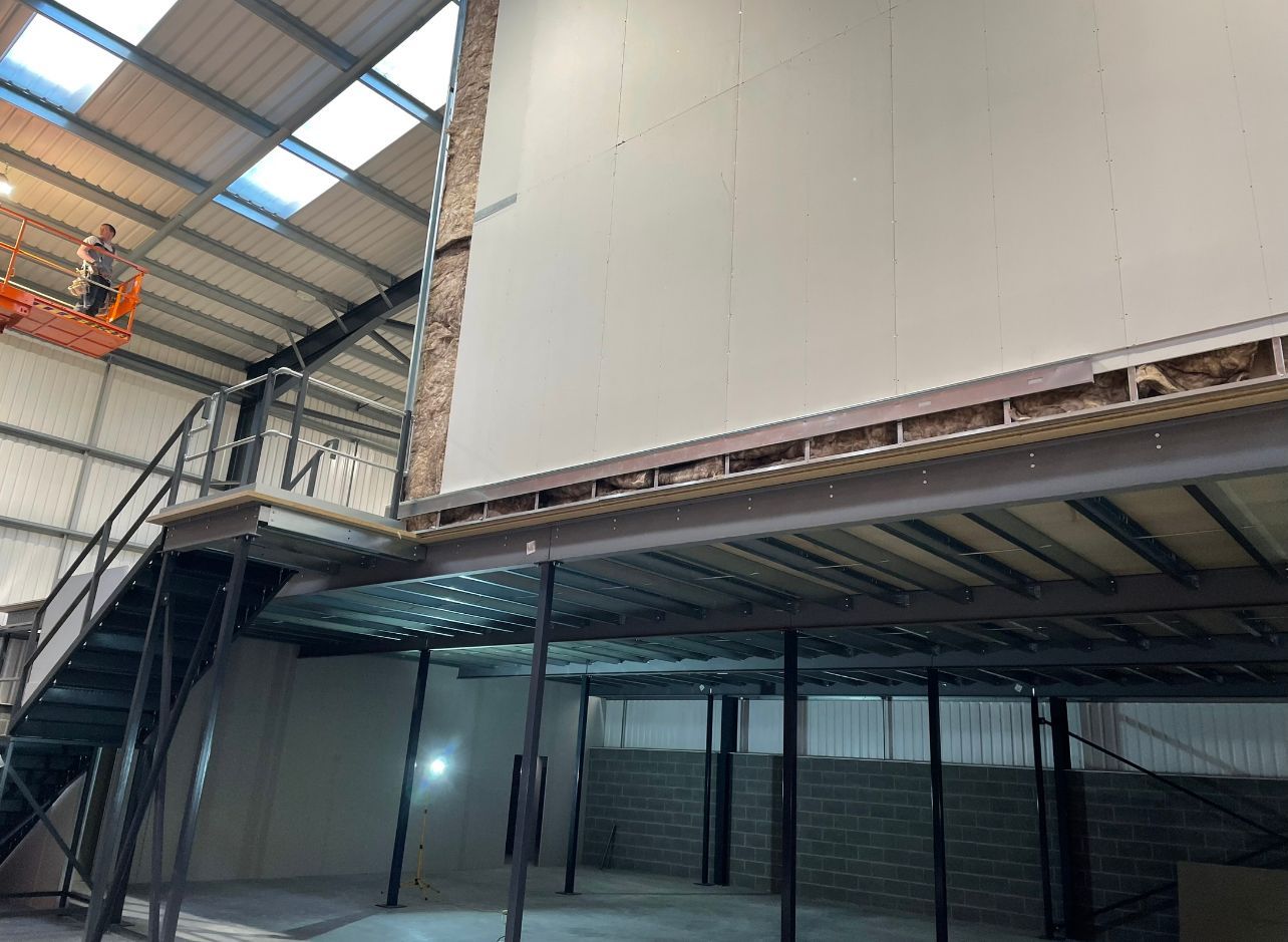 Empty industrial warehouse interior with metal beams, mezzanine, and large white wall paneling