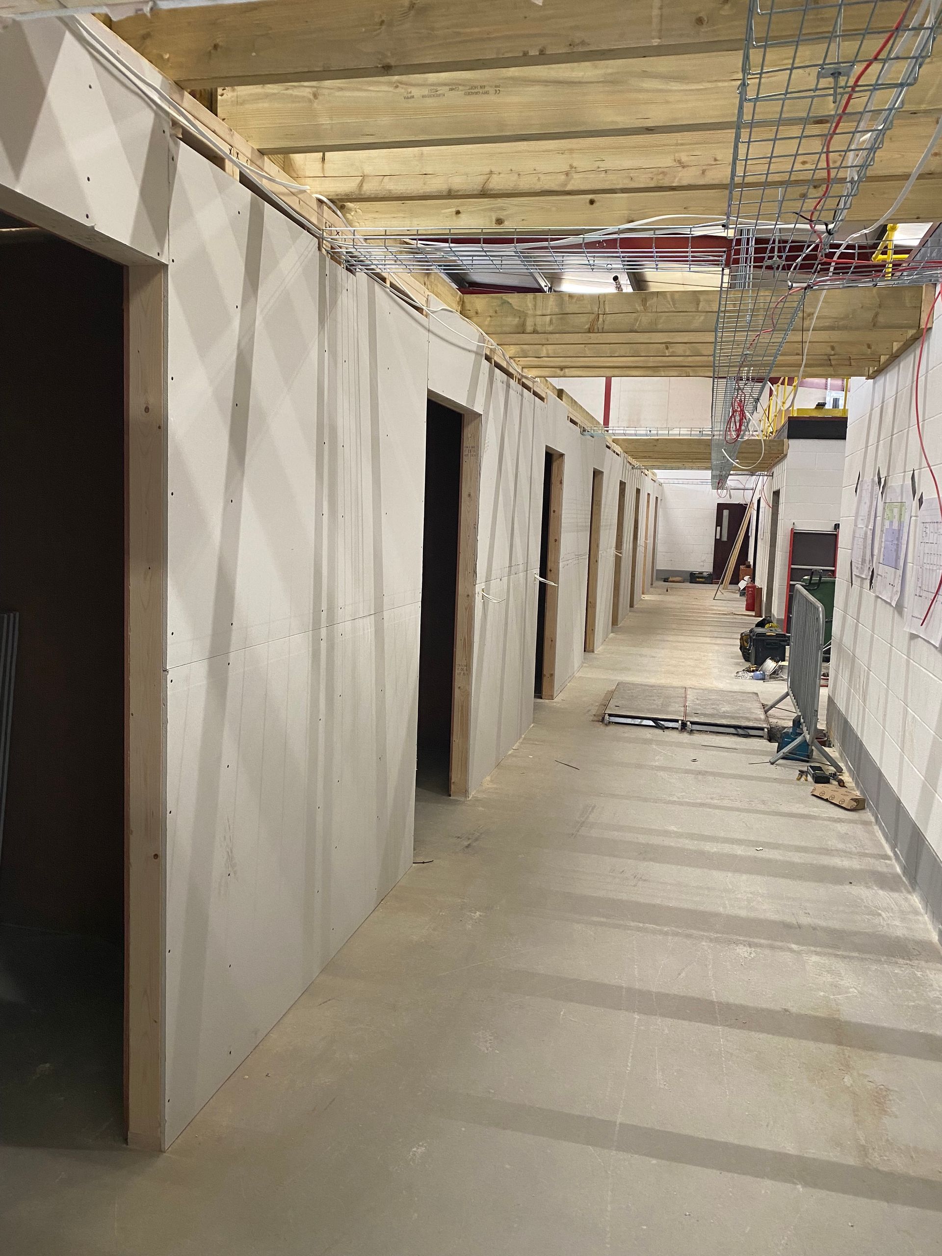 Narrow construction hallway with unfinished drywall, exposed ceiling, and tools in the distance