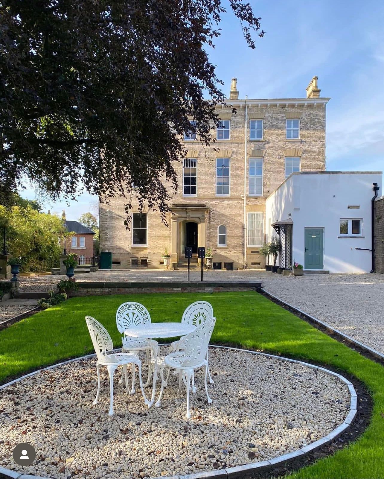 Courtyard with white patio furniture on gravel, leading to a stone manor house and small white annex.