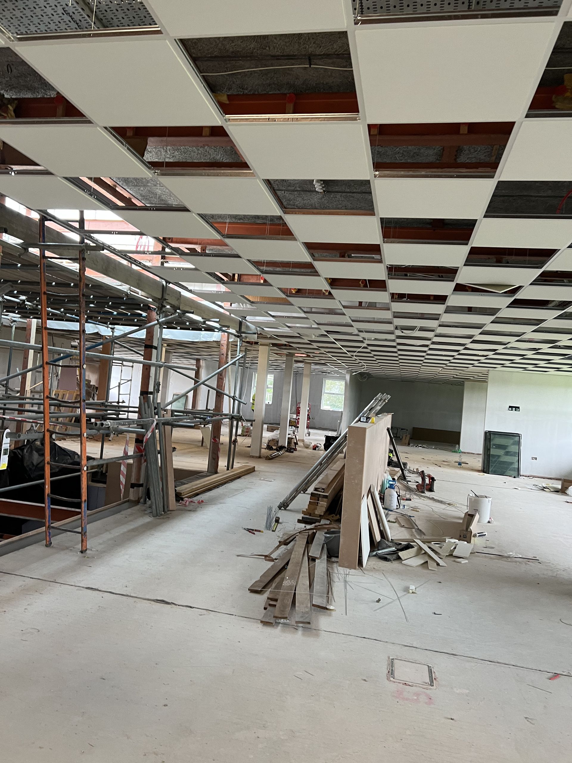 Renovation site with exposed ceiling tiles, scaffolding, and construction materials in an unfinished room