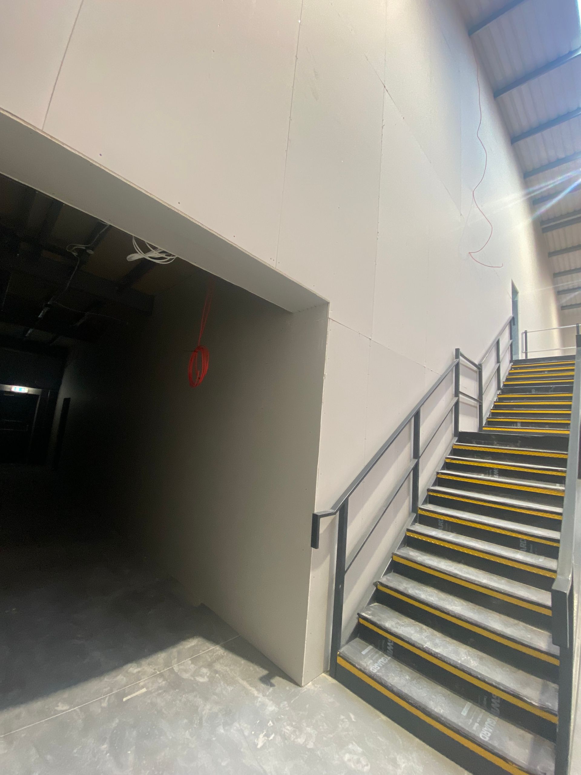 Indoor stairway with yellow-striped steps beside a dark loading-bay opening in an industrial building