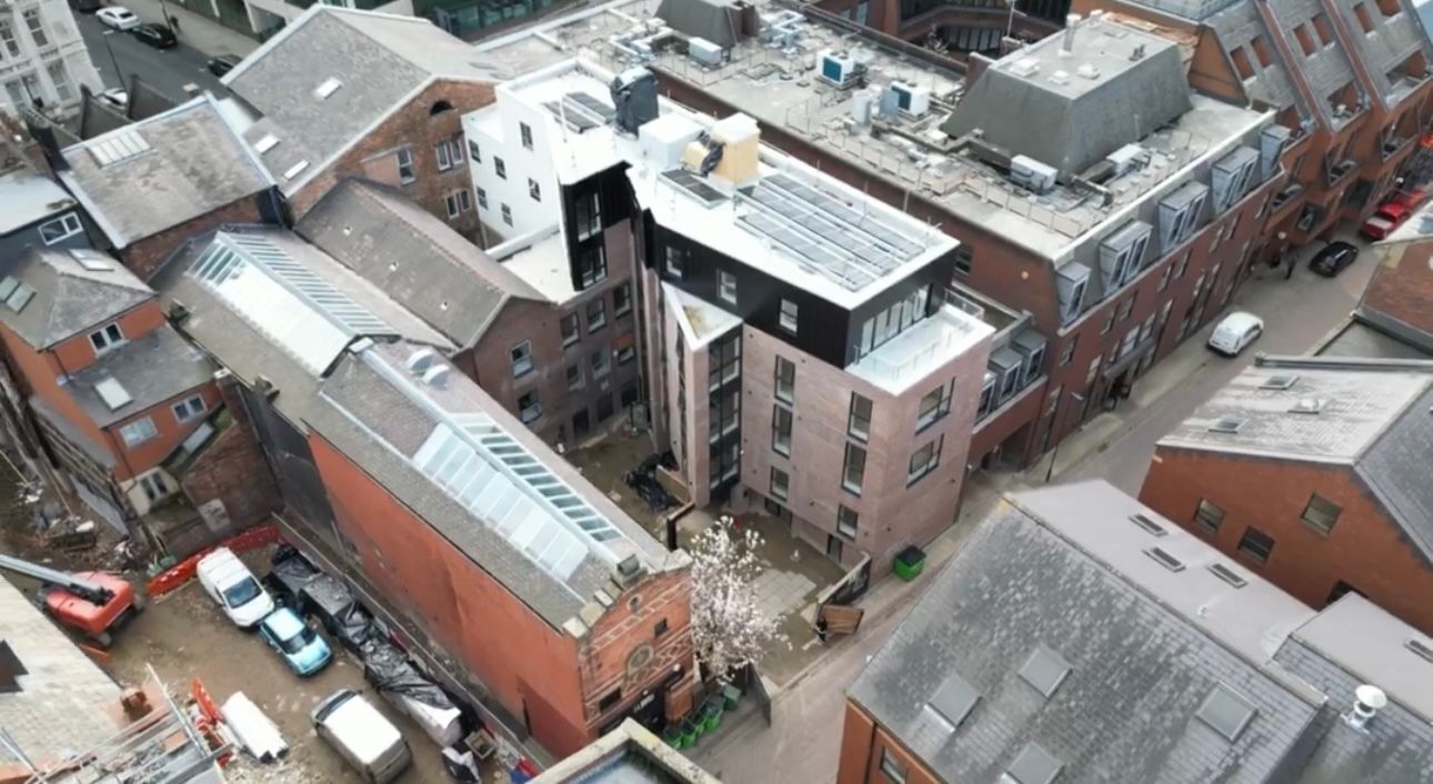 Aerial view of a city block with brick buildings, rooftops, and parked cars along narrow streets.