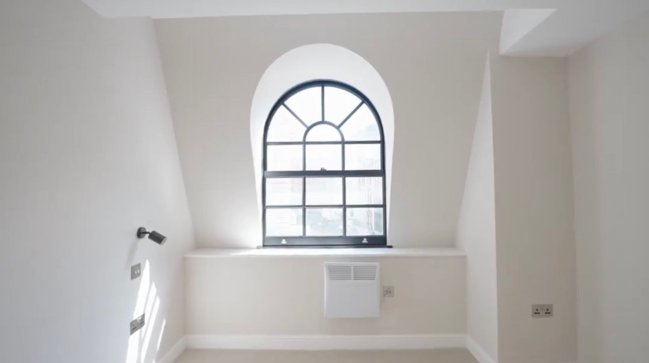 White room with an arched window, radiator below, and staircase railing on the left.