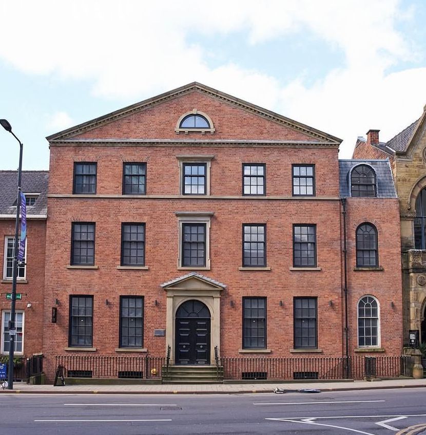 Red-brick historic building with arched doorway and many windows along a city street