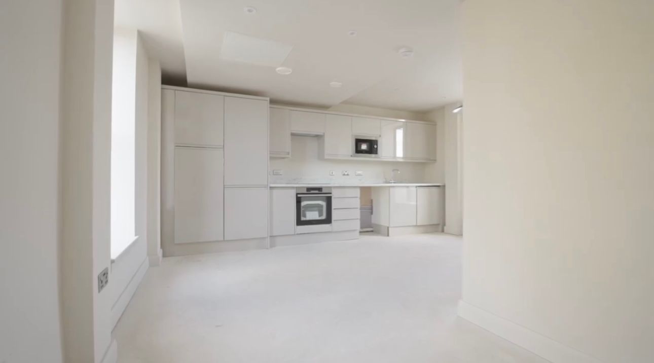 Bright empty modern kitchen with white cabinets, built-in oven, and an open living area.
