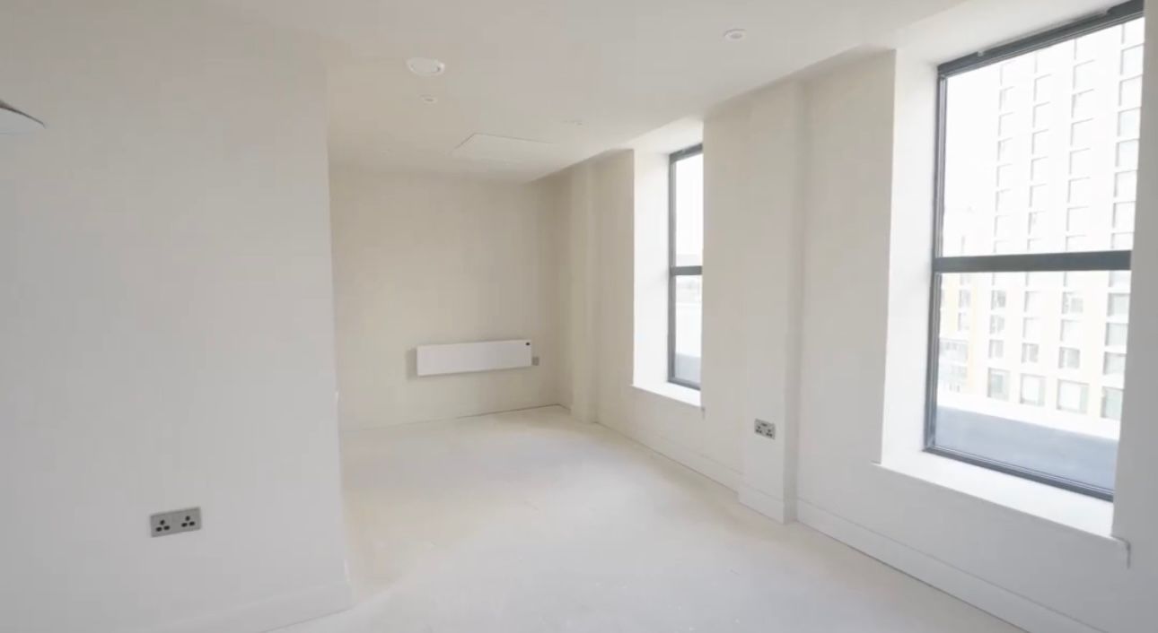Bright empty white room with large windows and a wall-mounted radiator.