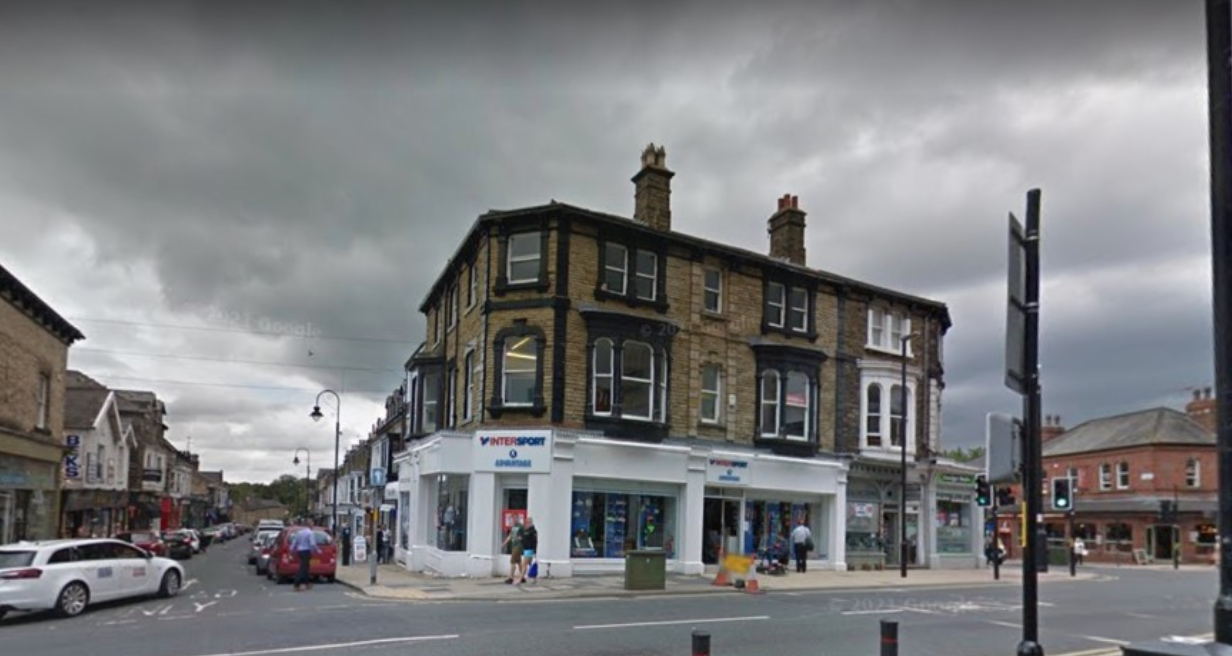 Street corner with a two-story stone building, shops at ground level, and cloudy sky overhead
