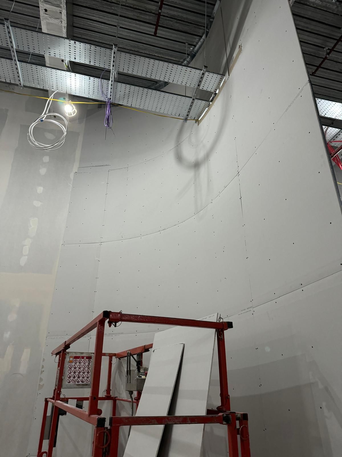 Scaffold and drywall panels inside a construction site with high ceiling and exposed lighting
