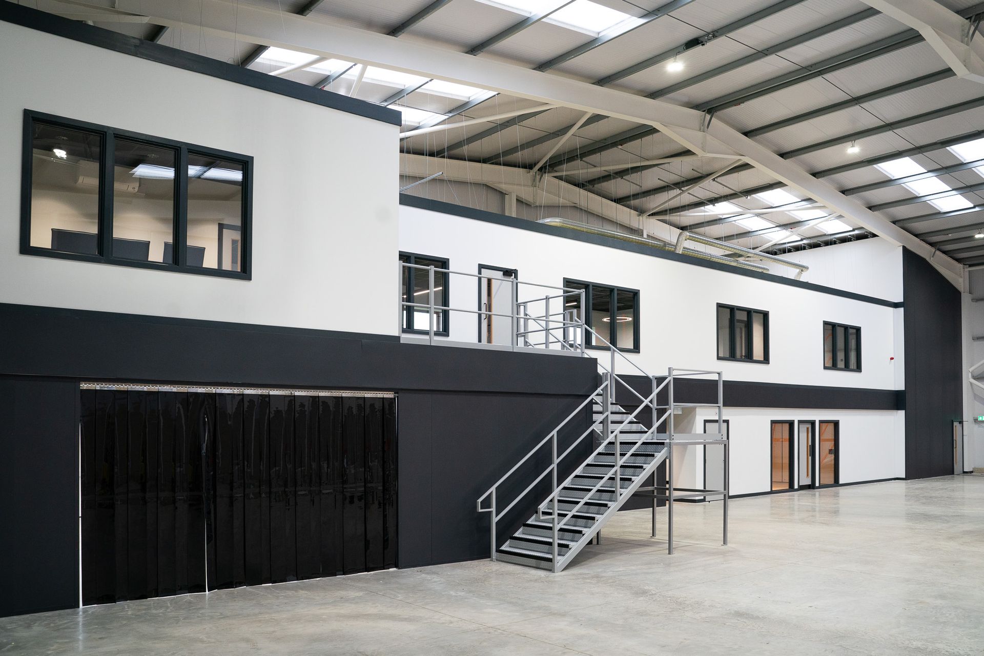 Empty industrial warehouse interior with mezzanine, metal stairs, and white-and-black walls