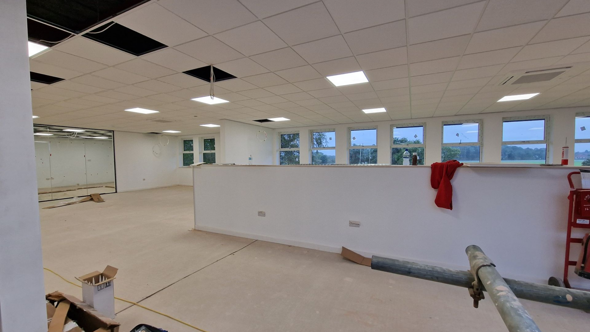 Interior of a room under construction with white walls, windows, and exposed ceiling panels.