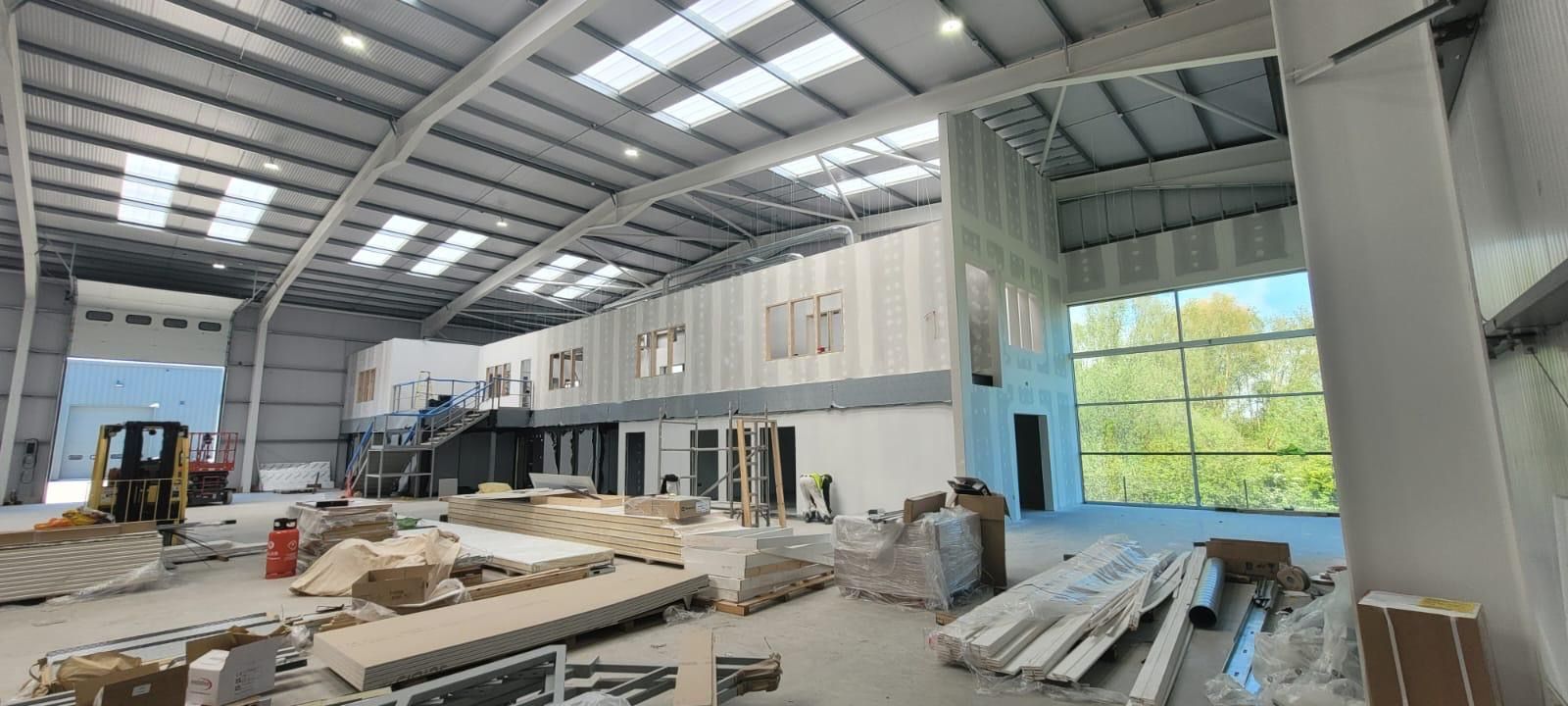 Partially built warehouse interior with metal roof, scaffolding, and construction materials scattered on the floor