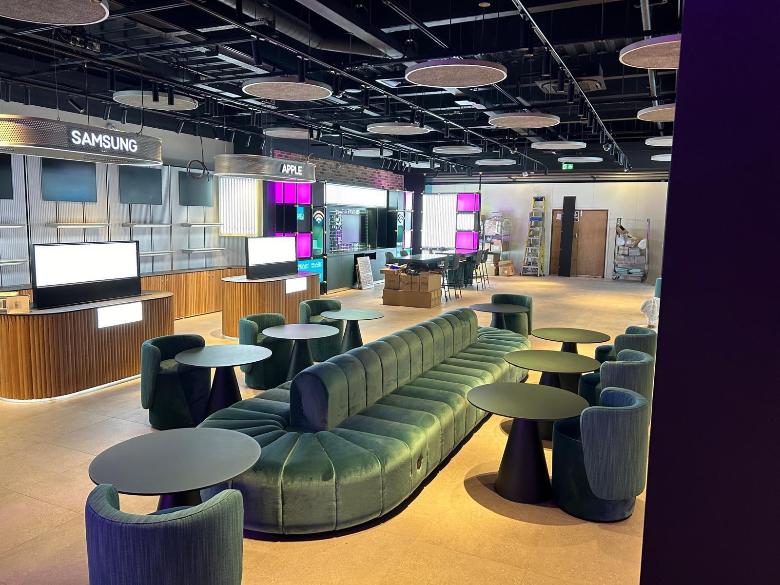 Modern lounge with green curved seating, round tables, and illuminated display screens in a spacious interior