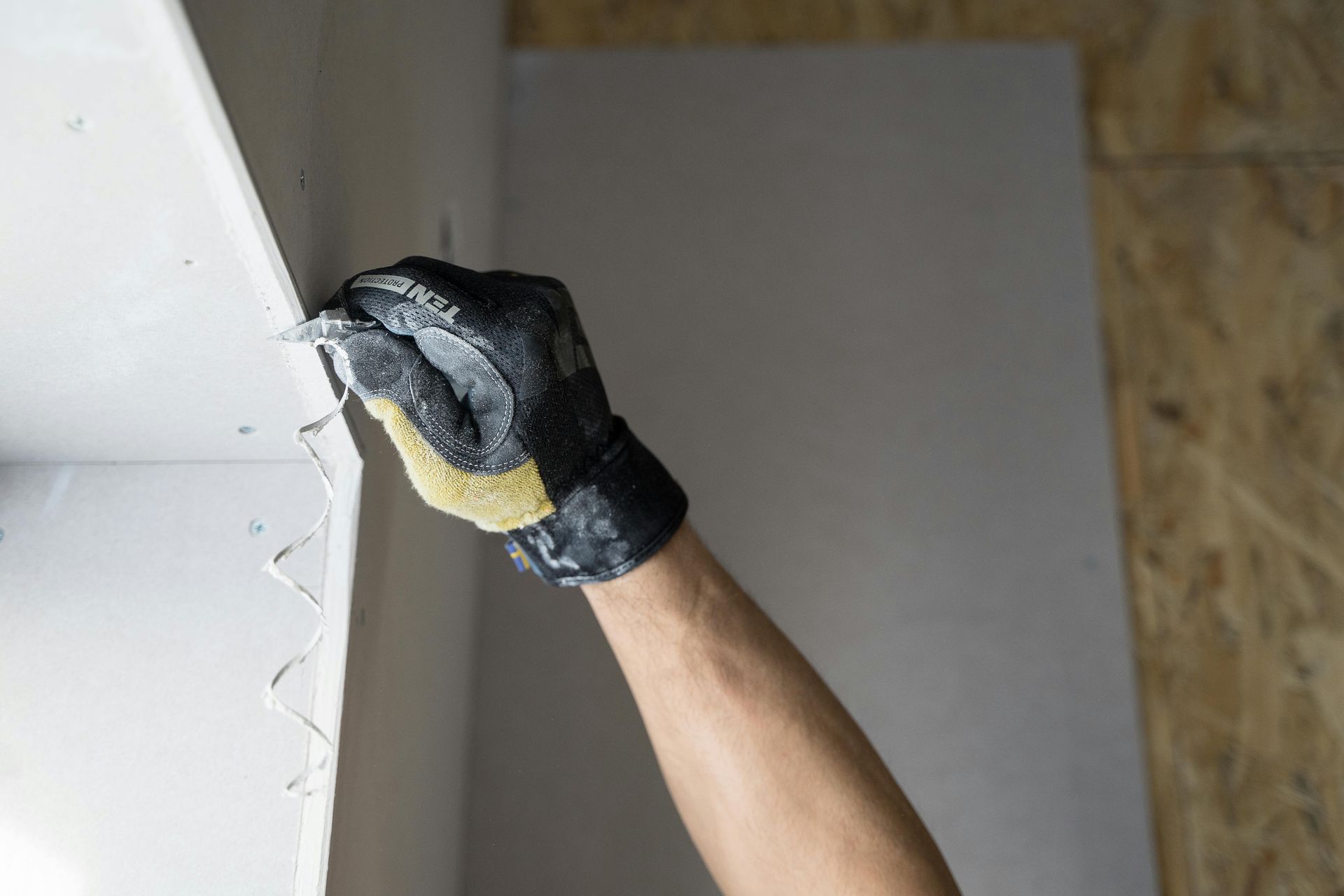 Gloved hand sanding the edge of a white drywall panel indoors