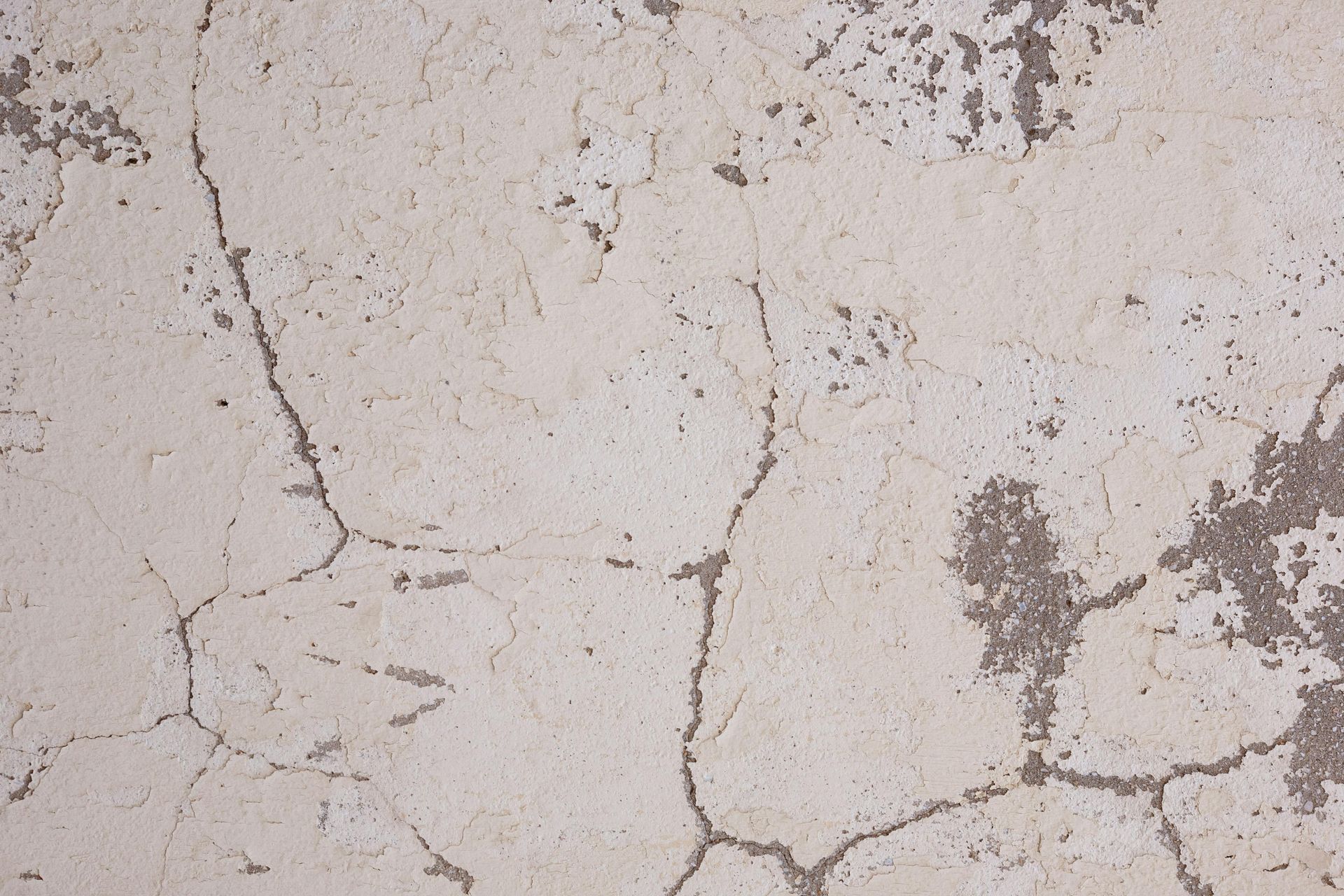 A light-colored, weathered concrete surface covered in a network of fine cracks and patches of textured gray wear.