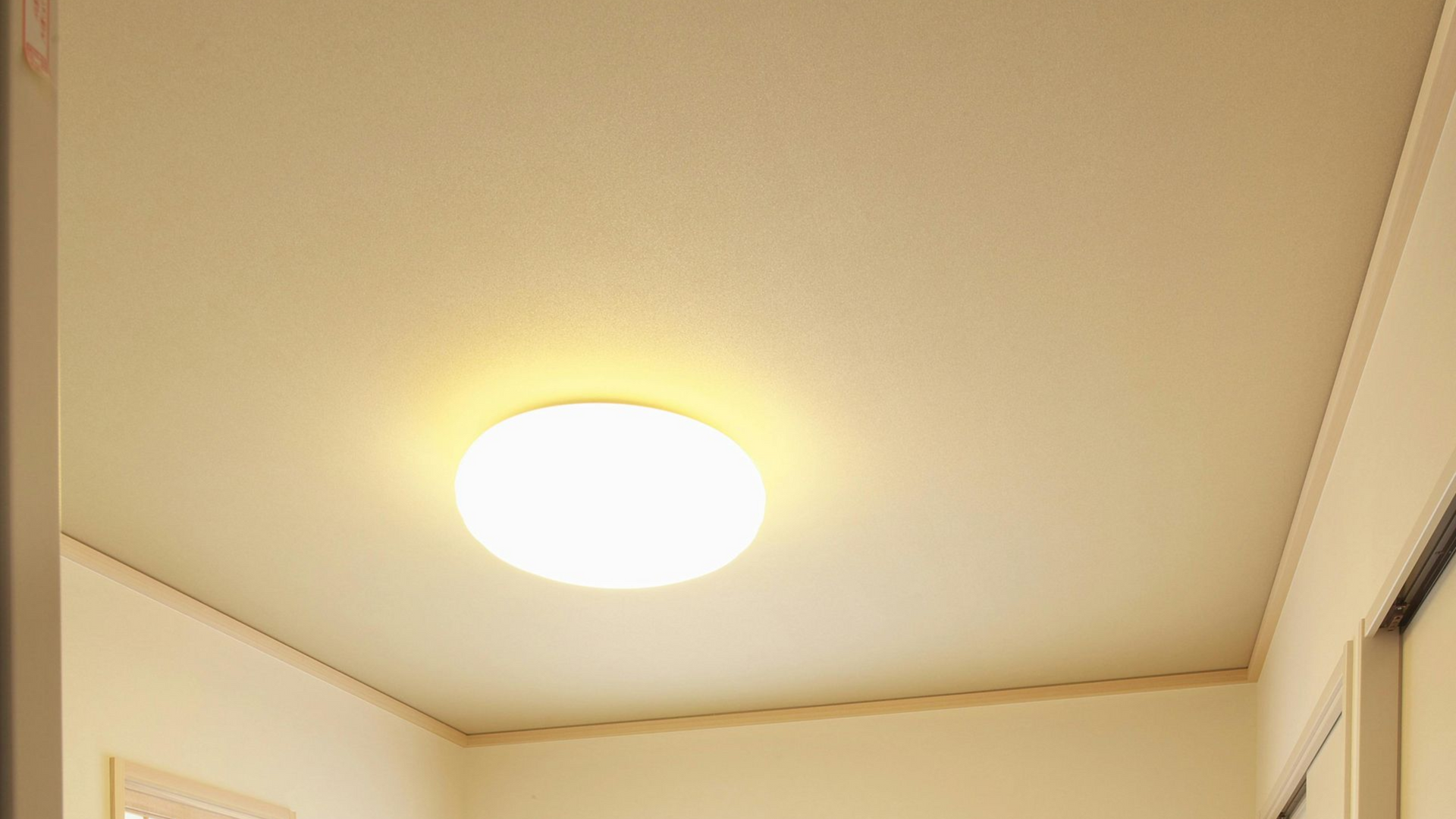 Ceiling with a bright, round light fixture. Walls are white and trimmed with wood.