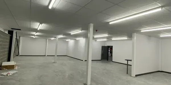Empty white industrial room with fluorescent lights, concrete floor, and support columns
