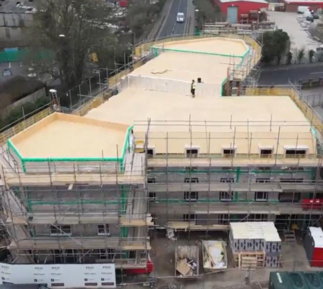 Aerial view of a building under construction with scaffolding and a light tan roof.