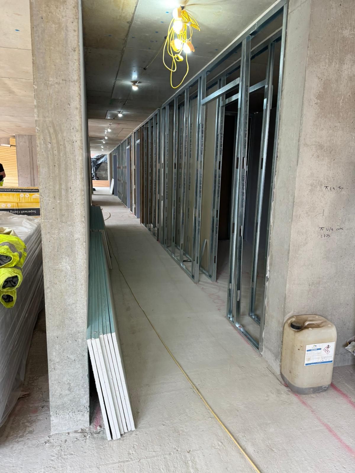 Partially framed indoor hallway with metal studs, concrete walls, and wiring overhead