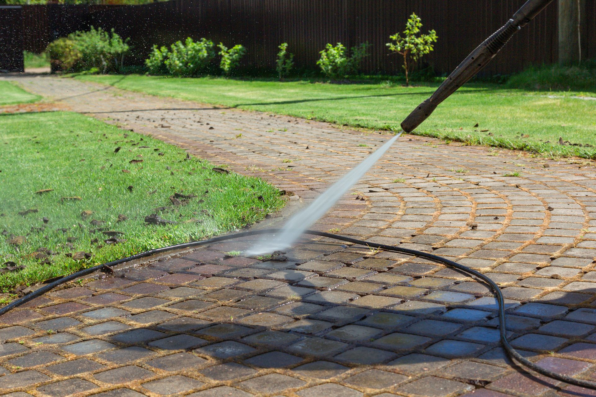 Power washer spraying water on a brick patio.