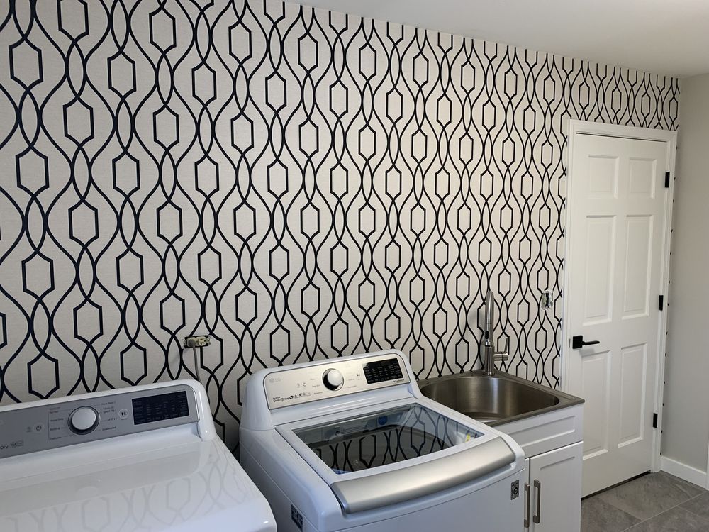 Laundry room with black and white geometric wallpaper, white appliances, and a utility sink.