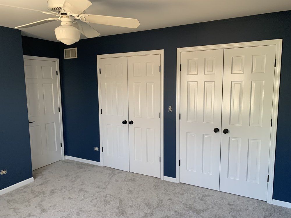Bedroom with navy blue walls, white doors, and gray carpet. A ceiling fan hangs overhead.