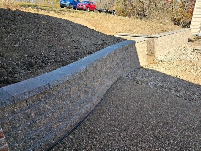 Retaining wall made of gray blocks. Dirt bank and gravel path are in front of the wall.